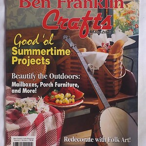 Peut inclure: Couverture de magazine Ben Franklin Crafts, avec un banjo, un panier de pique-nique et une nappe à carreaux rouges et blancs. Le texte de la couverture comprend "Good 'ol Summertime Projects" et "Redecorate with Folk Art!"