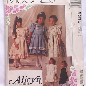 May include: McCall's sewing pattern for girls' dresses. The pattern features multiple dress designs, including a light pink dress with ruffles, a blue dress with lace trim, and a floral print dress. The pattern size is 3.