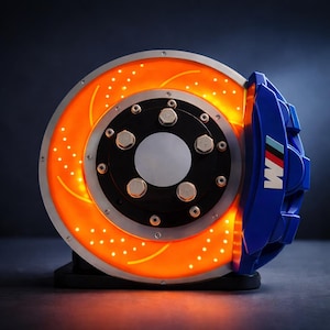 Peut inclure: Un disque de frein et un étrier de voiture éclairés. Le disque orange est percé de trous et bordé d'argent. L'étrier bleu affiche le logo BMW M. L'ensemble de frein est monté sur une base noire.