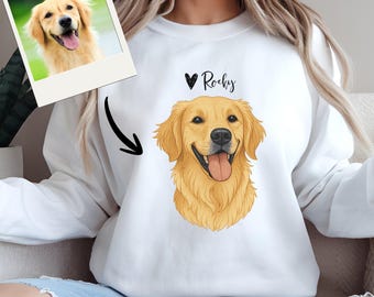 May include: White sweatshirt featuring a detailed illustration of a golden retriever dog with the name "Rocky" above it. A framed photograph of the dog is also present. The dog illustration is in shades of gold, brown, and black.