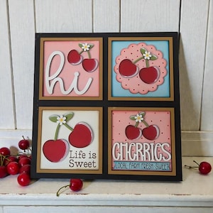 May include: A decorative wooden sign featuring four square panels with cherry designs. The panels have a black frame and include the words "hi", "Life is Sweet", and "CHERRIES". The cherries are red with green stems and white flowers.