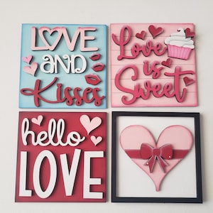 May include: Four wooden signs with Valentine's Day themes. The signs feature the phrases "Love and Kisses", "Love is Sweet", "Hello Love", and a pink heart with a red bow.