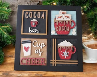 May include: A black framed wall art piece with four square panels. Each panel features a cocoa-themed design with text like "COCOA Bar" and "Cup of CHEER". The designs include mugs, marshmallows, and a to-go cup with a heart.