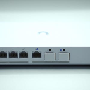 Peut inclure: Un appareil réseau blanc avec des supports d'angle noirs. L'appareil dispose de plusieurs ports Ethernet, de voyants lumineux et d'une entrée d'alimentation. La surface supérieure présente un logo subtil.
