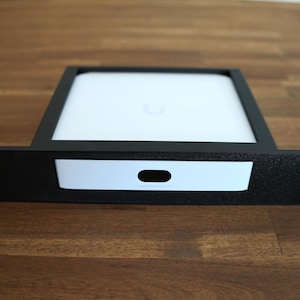 May include: Black metal rack mount with a white device inside. The device has a white face with a black oval cutout. The rack mount has mounting holes on each side. The device is likely for networking or data storage.