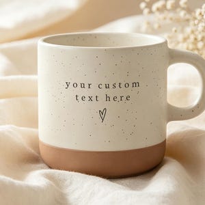 Op de afbeelding: Een keramische mok met een gespikkeld crèmekleurig bovengedeelte en een effen terracotta-kleurige basis. De mok is voorzien van de zwarte tekst your custom text here en een klein handgetekend hartsymbool onder de tekst op de voorzijde.