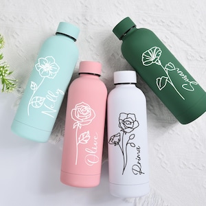 Könnte beinhalten: Vier isolierte Wasserflaschen in Pastellfarben: Türkis, Rosa, Weiß und Grün. Jede Flasche hat ein Blumendesign und einen Namen in Schreibschrift. Die Flaschen sind auf einer weißen Oberfläche mit Grün angeordnet.