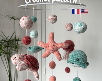 May include: A crochet mobile with sea-themed creatures and spheres in pink, teal, and white. The mobile includes a starfish, turtle, whale, and jellyfish, suspended from a white ring. The text "Crochet pattern" is visible.