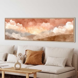 Könnte beinhalten: Ein rechteckiges, gerahmtes Leinwandkunstwerk, das eine Landschaft in warmen Farbtönen zeigt. Das Kunstwerk zeigt einen Himmel mit Pfirsich-, Orange- und Weißtönen über einer braunen und grauen Landschaft. Das Kunstwerk wird über einem beigen Sofa ausgestellt.