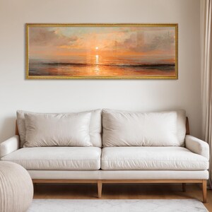 May include: A panoramic landscape painting depicting a sunset over the ocean, framed in a thin gold border. The artwork features warm orange and golden hues reflecting on the water surface, with soft clouds in the sky above the horizon line.