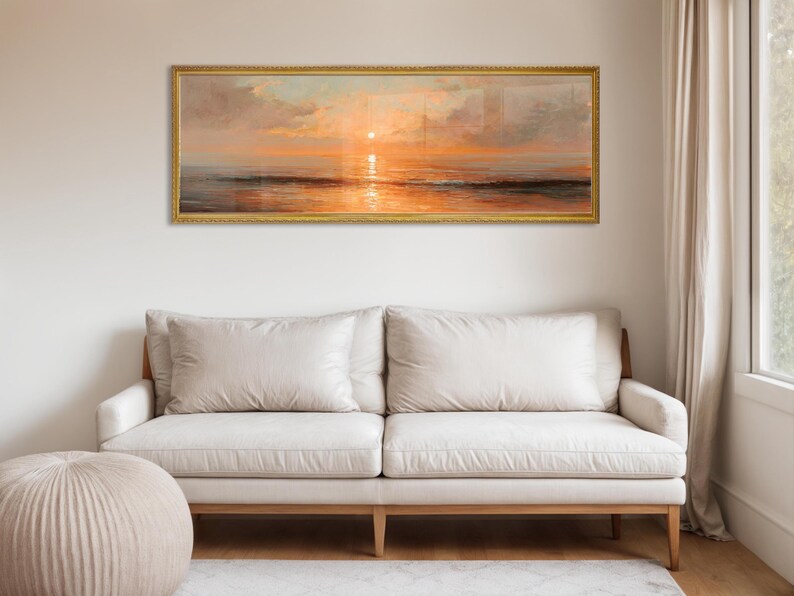 May include: A panoramic landscape painting depicting a sunset over the ocean, framed in a thin gold border. The artwork features warm orange and golden hues reflecting on the water surface, with soft clouds in the sky above the horizon line.