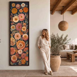 May include: A tall, rectangular framed wall art piece featuring a dense, vertical arrangement of blooming flowers in shades of orange, pink, yellow, and cream against a dark navy blue background, encased in a thin, dark brown wooden frame.