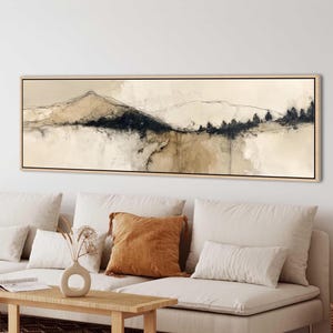 Puede incluir: Impresión artística de paisaje abstracto en un marco de madera rectangular. La obra presenta una cordillera con tonos azul oscuro y beige. La pintura se exhibe sobre un sofá blanco con cojines y una mesa de centro de madera.