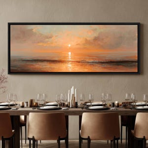 May include: A panoramic landscape painting in a black frame depicting a sunset over the ocean. The sky is filled with soft orange and peach clouds, while the sun reflects brightly on the calm water surface, creating a warm, glowing horizon line.
