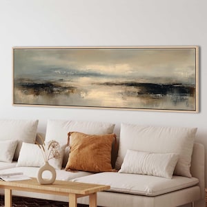 Peut inclure: Peinture de paysage abstrait dans un cadre rectangulaire en bois clair. L'œuvre présente des tons sourds de beige, de gris et de bleu marine, créant une scène sereine et atmosphérique. Le tableau est au-dessus d'un canapé blanc.