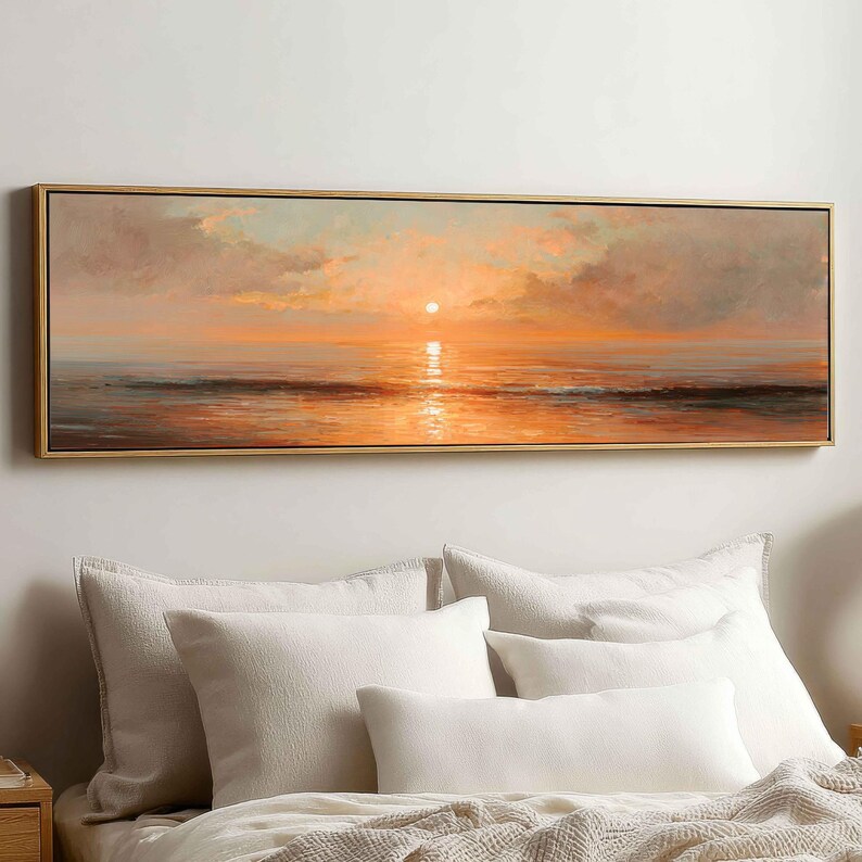 May include: A panoramic landscape painting in a thin gold frame depicting a sunset over a calm ocean. The sky and water are filled with warm orange, peach, and soft grey tones, with the sun appearing as a bright white circle above the horizon.