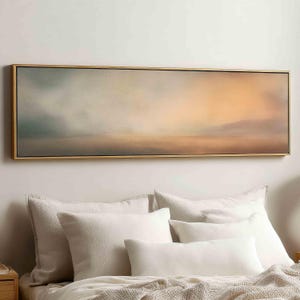 Puede incluir: Una pieza de arte mural rectangular panorámica que presenta un paisaje abstracto con degradados suaves y difuminados en tonos azul verdoso apagado, melocotón cálido y beige. La obra está enmarcada en un fino marco de metal dorado.