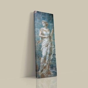 May include: A tall, rectangular canvas print featuring a classical statue of a figure in a draped white gown holding a bow. The artwork displays a weathered, blue-toned background with textured, distressed details and subtle gold accents on the clothing.