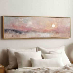 May include: A panoramic landscape painting in a thin gold frame featuring a textured, abstract sunset scene with soft pink, peach, and muted grey tones. A bright white circular sun sits above a hazy horizon line over a light, neutral foreground.