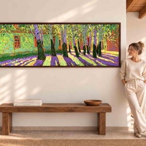 Puede incluir: Un cuadro panor&aacute;mico de paisaje en un marco de madera oscura que muestra una hilera de &aacute;rboles con hojas verdes y troncos oscuros que proyectan largas sombras p&uacute;rpuras sobre un suelo amarillo brillante, junto a un edificio verde con marcos rojos.