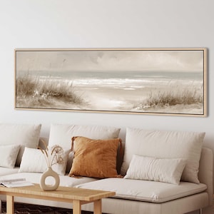 Puede incluir: Una pintura de paisaje panorámico en un marco de madera clara que representa una escena costera con dunas de arena, hierba alta de playa y un océano tranquilo bajo un cielo suave y nublado. La obra presenta una paleta de colores neutros.