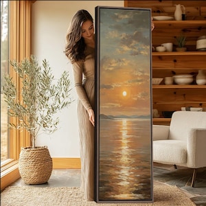 Puede incluir: Un cuadro en lienzo enmarcado, alto y rectangular, que representa una puesta de sol sobre un cuerpo de agua en calma. La obra presenta tonos dorados y anaranjados cálidos que se reflejan en el agua, con nubes suaves sobre colinas lejanas.