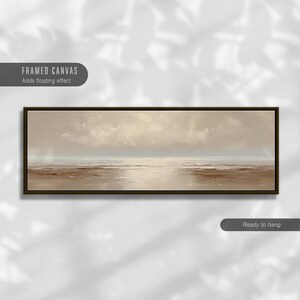 May include: A framed canvas art piece depicting a serene seascape. The artwork features a muted color palette of beige, brown, and white, with a dark brown frame. The text "FRAMED CANVAS Adds floating effect" is visible.