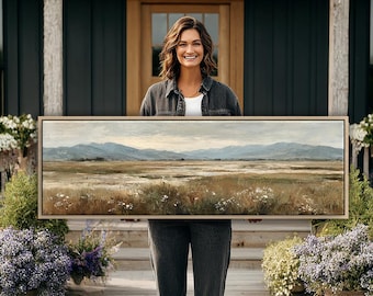 Puede incluir: Un cuadro de paisaje rectangular en un marco de madera clara que muestra un campo amplio y plano con parches de flores silvestres blancas en primer plano, hierbas secas y montañas azuladas bajo un cielo nublado.