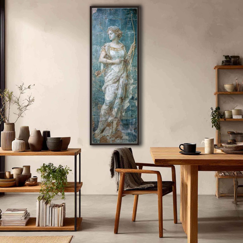 May include: A vertical rectangular wall art piece featuring a classical painting of a figure in a flowing white gown holding a bow. The artwork has a distressed, weathered texture with blue and gold tones, framed in a thin dark brown border.