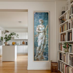 May include: A tall, rectangular framed wall art piece featuring a classical figure in a white draped garment holding a bow. The artwork has a weathered, distressed blue and gold finish with visible grid lines, presented in a light wood frame.