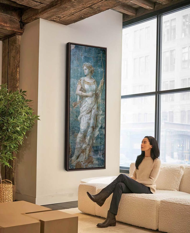 May include: A tall, rectangular framed wall art piece featuring a classical painting of a figure in a flowing white and gold garment holding a bow. The artwork has a distressed, weathered texture with blue and earthy brown tones in a dark frame.