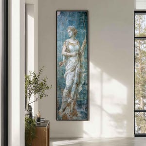 May include: A tall, rectangular wall art piece featuring a classical figure in a flowing white gown against a distressed, textured blue background. The figure holds a long, thin bow, with a quiver of arrows visible at the hip, framed in a thin black border.