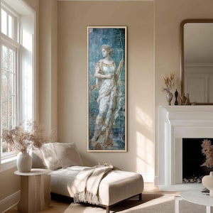 May include: A tall, rectangular framed wall art piece featuring a classical-style figure holding a bow, rendered in shades of blue, white, and gold. The artwork is displayed in a thin, light-colored wooden frame, showcasing a vertical composition.