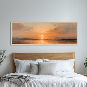May include: A panoramic landscape painting of a sunset over the ocean, featuring warm orange and golden hues reflecting on the water surface, with soft clouds in the sky, all enclosed within a thin, light-colored wooden frame.