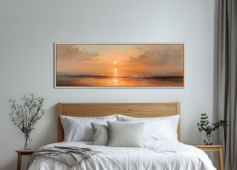 May include: A panoramic landscape painting of a sunset over the ocean, featuring warm orange and golden hues reflecting on the water surface, with soft clouds in the sky, all enclosed within a thin, light-colored wooden frame.