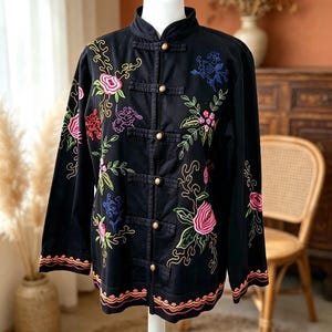 May include: A black long-sleeved jacket featuring a mandarin collar and five gold-toned spherical buttons. The jacket is decorated with colourful floral embroidery in shades of pink, red, green, and blue, with wavy orange and pink trim at the hem.