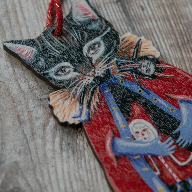 Peut inclure: Un chat noir portant un uniforme rouge et bleu avec un col blanc et une bordure dor&eacute;e. Le chat tient une petite figurine blanche avec un chapeau rouge et un manteau bleu. Le chat tient un instrument de musique.