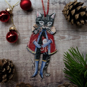 Peut inclure: Un chat noir portant un manteau rouge et bleu avec des garnitures dor&eacute;es tient une petite poup&eacute;e. Le chat est une d&eacute;coration de No&euml;l avec une ficelle pour l'accrocher.