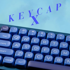 May include: Close-up of a blue mechanical keyboard with white lettering. The keys are a darker shade of blue, and the background is a lighter blue. The word "KEYCAP X" is written in blue across the top.