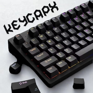 May include: Black mechanical keyboard with illuminated keys. The keyboard has the text "KEYCAPX" in white. The keys are black with white lettering and symbols. A Shift key and a PgUp key are detached from the keyboard.