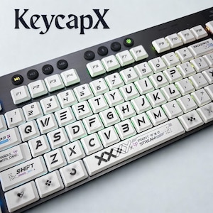 Puede incluir: Un teclado de ordenador negro con teclas blancas y letras negras. El texto "KeycapX" es visible en la parte superior. Algunas teclas tienen símbolos y texto adicionales, incluyendo "PRINT x Ø STREAM".