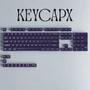 May include: A set of dark purple keyboard keycaps, arranged on a light gray surface. The keycaps are labeled with white lettering and symbols. The word "KEYCAPX" is displayed in large black letters above the keycaps.