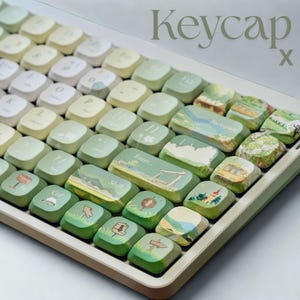 Könnte beinhalten: Eine Tastatur mit individuellen Tastenkappen. Die Tastenkappen sind ein Farbverlauf aus Grün und Weiß, wobei einige Tasten Landschaftsillustrationen aufweisen. Der Text "Keycap x" befindet sich in der oberen rechten Ecke.