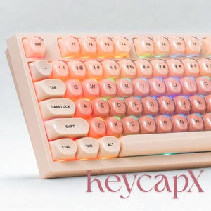 May include: A close-up of a mechanical keyboard with light pink keycaps and a matching frame. The keys are arranged in a standard layout with white lettering. The keyboard has a retro aesthetic, with the text "keycapx" in a cursive font at the bottom.