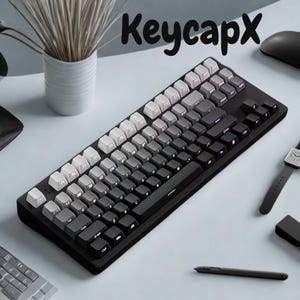 May include: A black mechanical keyboard with a gradient keycap design, transitioning from white to gray to black. The keyboard has the text "KeycapX" in the upper right corner. Other items on the desk include a mouse, watch, and pen.