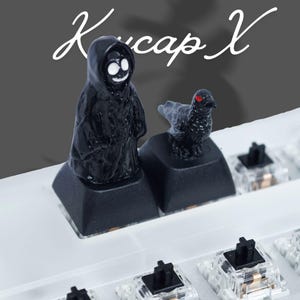 May include: Black custom keycaps featuring a Grim Reaper figure and a bird with red eyes. The keycaps are mounted on a white keyboard. The text "Keycap X" is in the background.