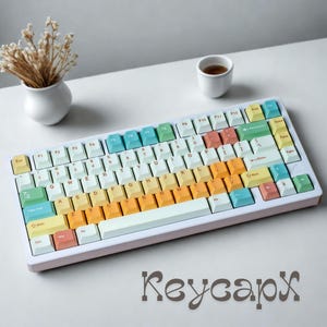 May include: A pastel-colored mechanical keyboard with a white frame and gradient keycaps. The keycaps transition from yellow to orange, with accents of blue, green, and pink. The word "Keycapx" is written in a decorative font at the bottom.