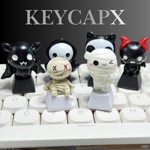 Puede incluir: Un conjunto de teclas decorativas con personajes espeluznantes, como un murciélago, una parca, un panda, una momia y un diablo. Las teclas son negras, blancas y beige, y se muestran en un teclado blanco. La palabra "KEYCAPX" está impresa en la parte superior.