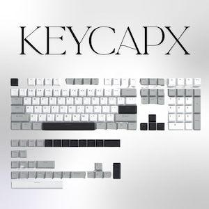 May include: A collection of white and grey keycaps with black accents, displayed on a white background. The word "KEYCAPX" is written in large black letters above the keycaps. The keycaps are for a mechanical keyboard.