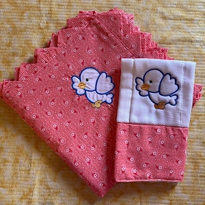 May include: A set of pink and white fabric napkins with embroidered birds. The napkins have a paisley pattern and are folded in a stack.